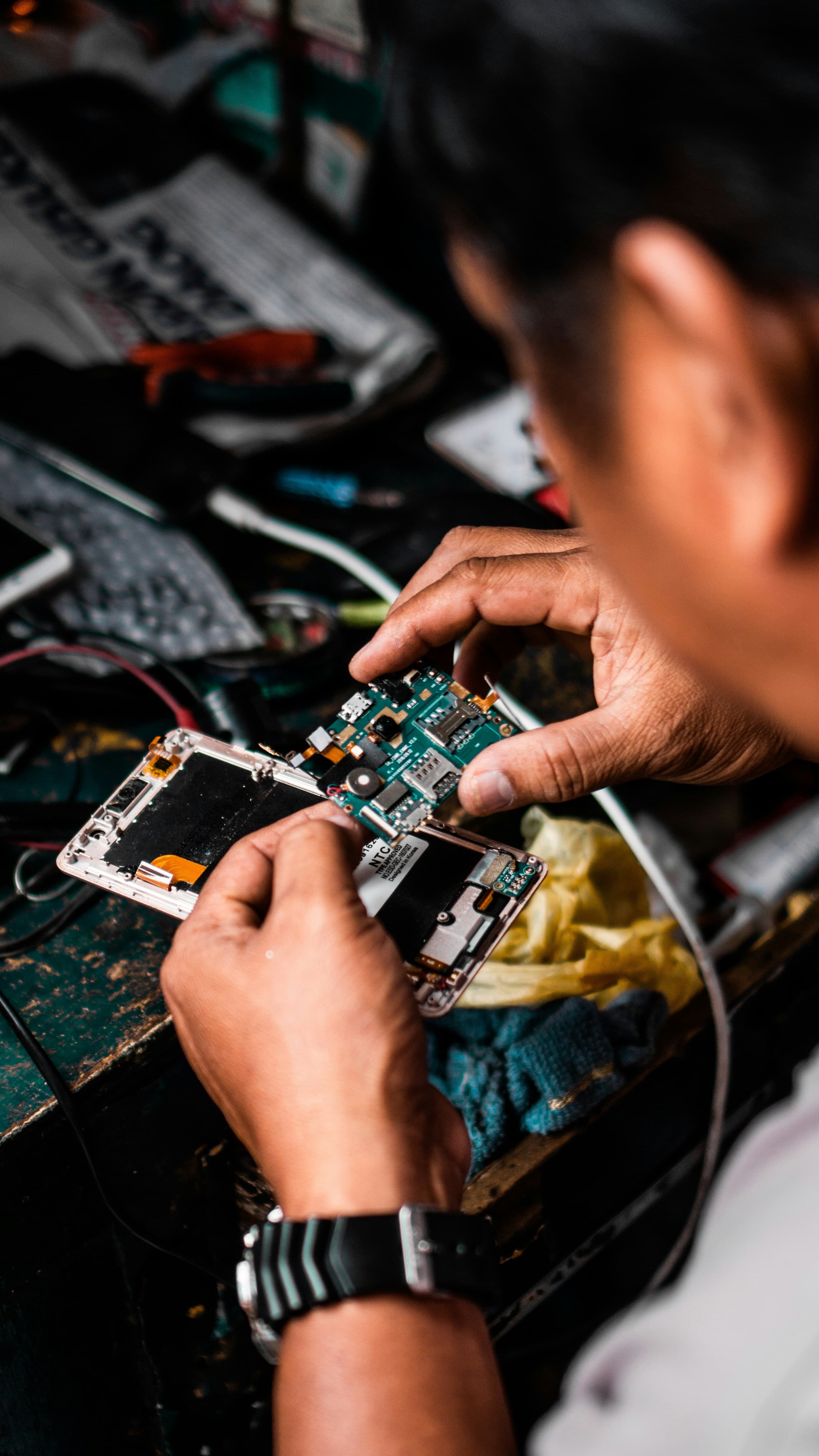 Hands lifting the circuit board out of an opened smartphone on a technician's workbench
