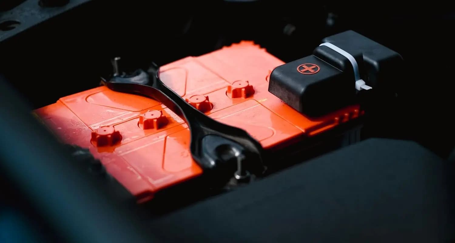 An orange lead-acid battery with its terminal cover, held down by a bracket